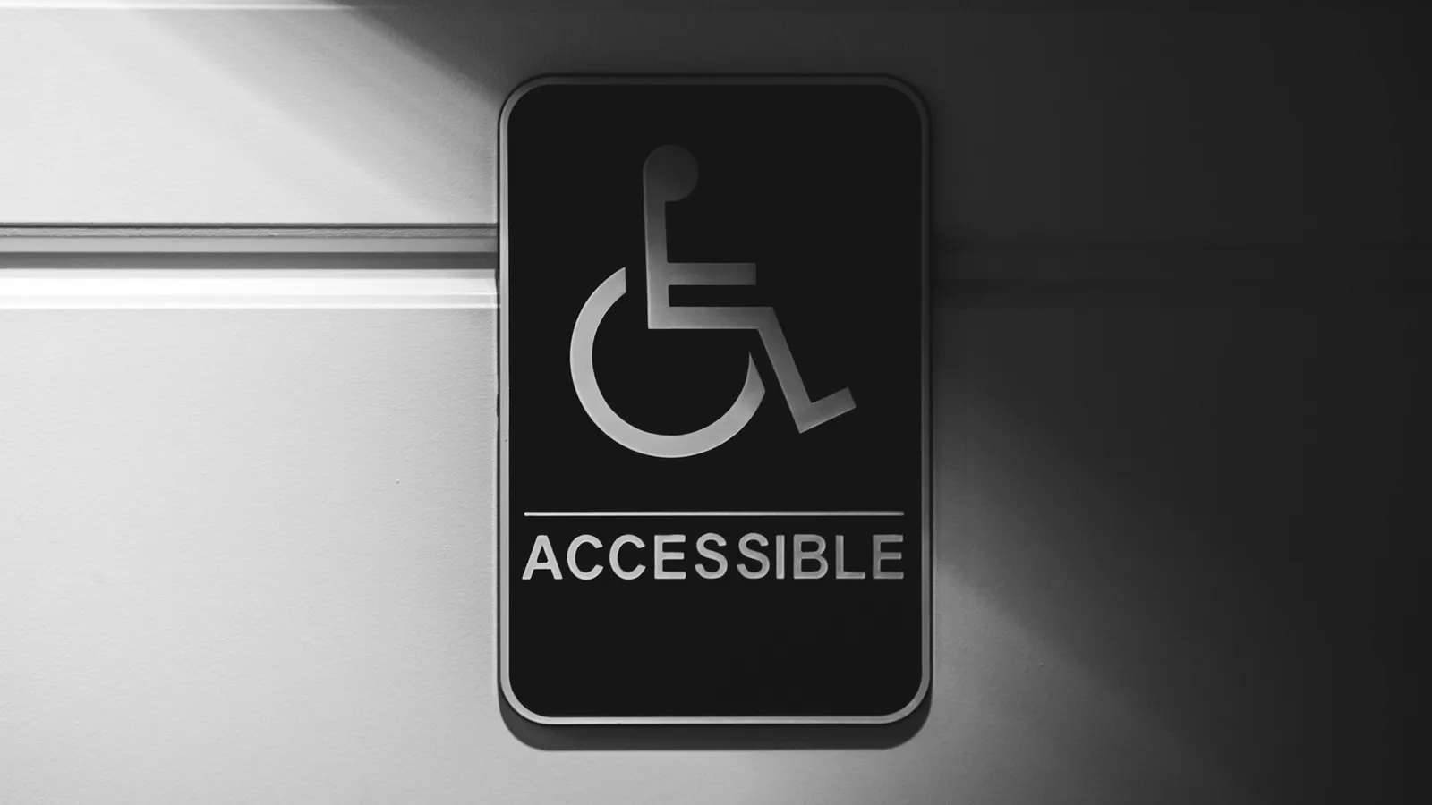 Accessible signage indicating an accessible route, used here as a metaphor for environments that are designed to fit people, rather than asking people to bend themselves to fit the environment.