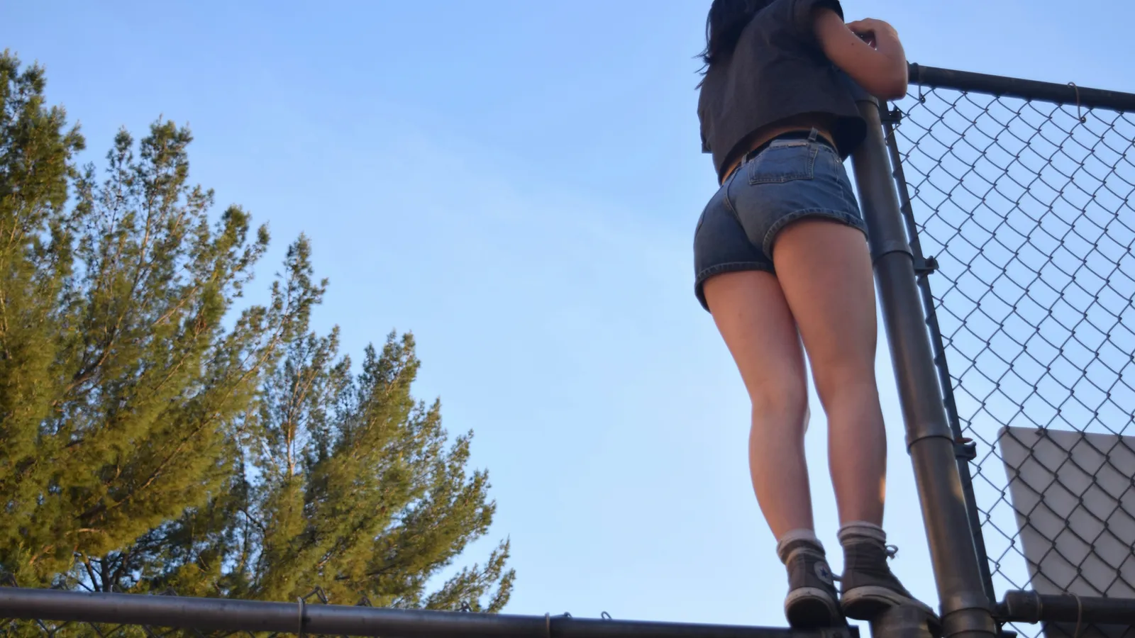 A young woman climbing a fence outside, used here to evoke the way ADHD-associated traits seek out novelty and exploration in environments that often were not built to accommodate them.