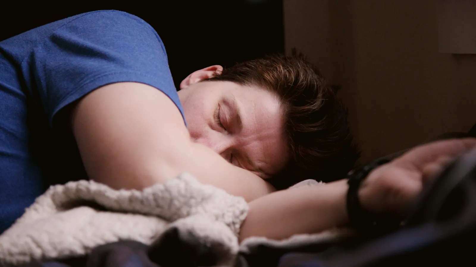 A man lying on his side under a blanket, resting with his eyes closed.