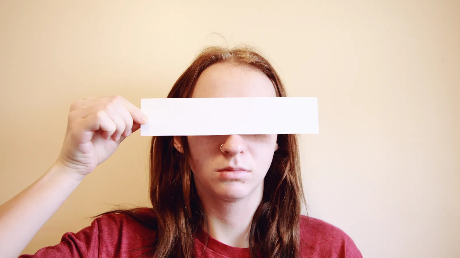 A woman holding a blank strip of paper across her eyes.