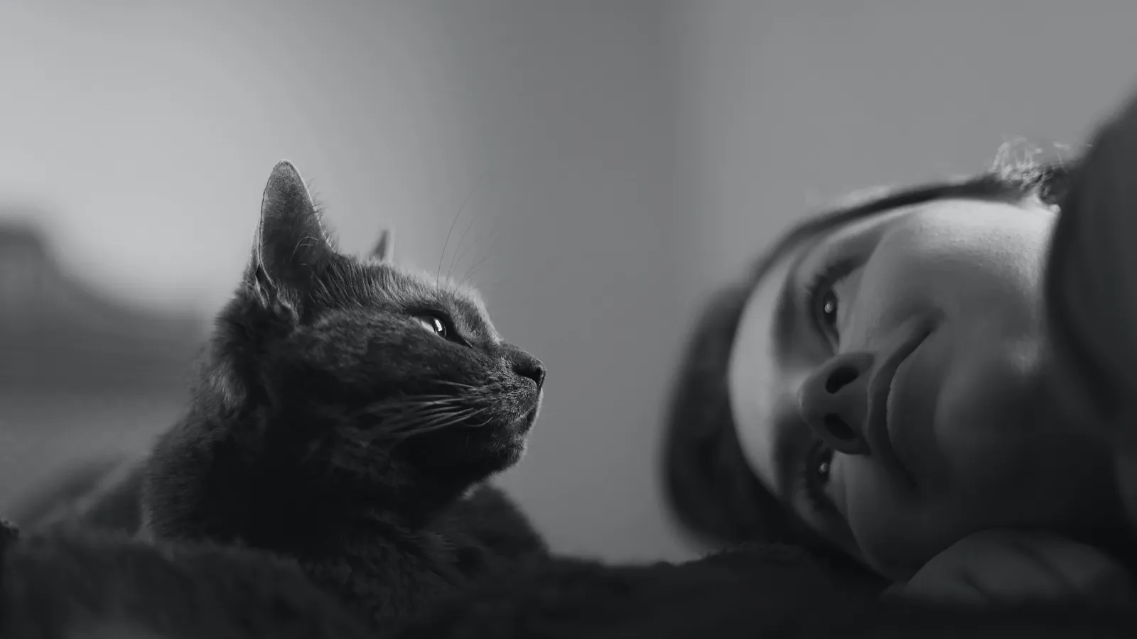 Black-and-white photo of a woman lying beside a cat, both looking the same way.