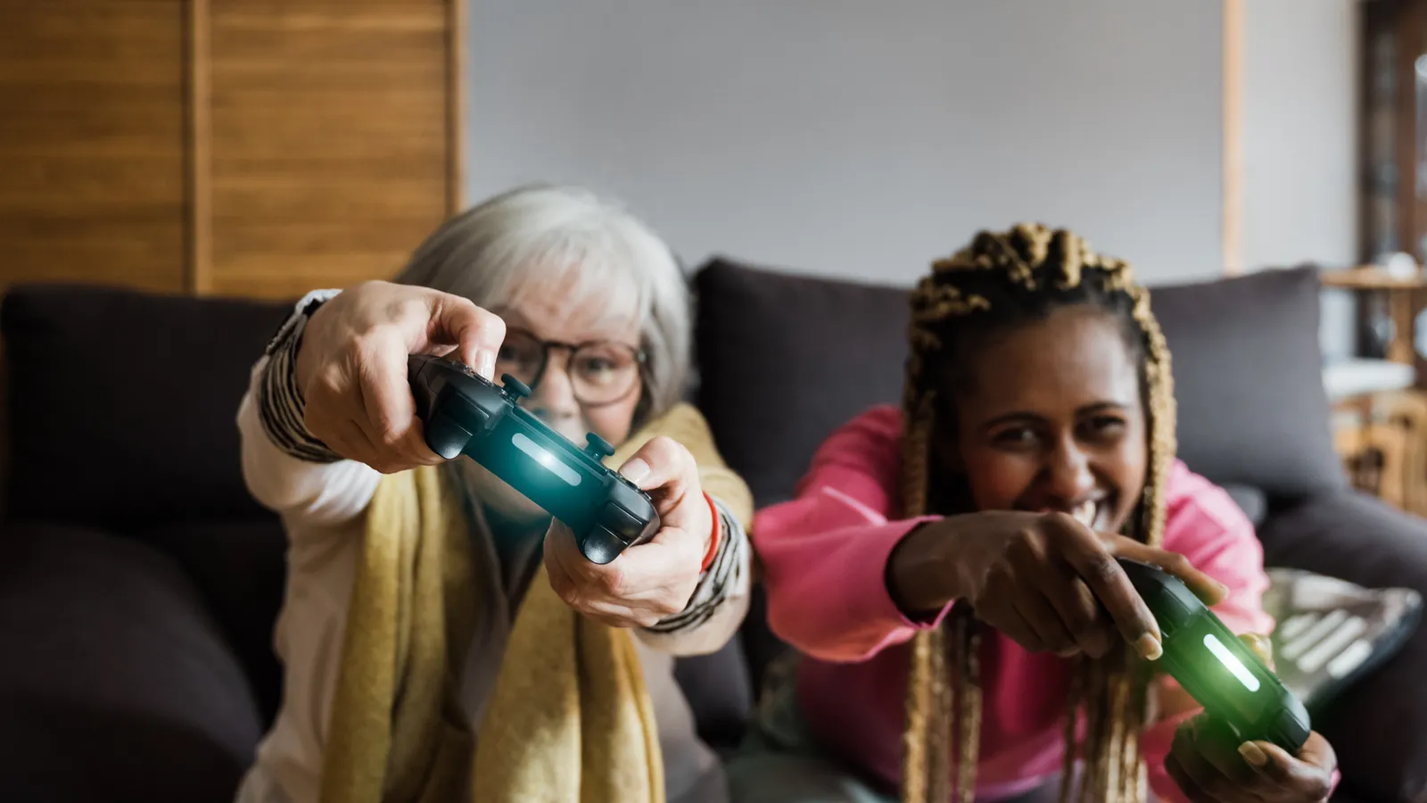 An older woman and a younger woman laughing as they play a video game together on a couch.