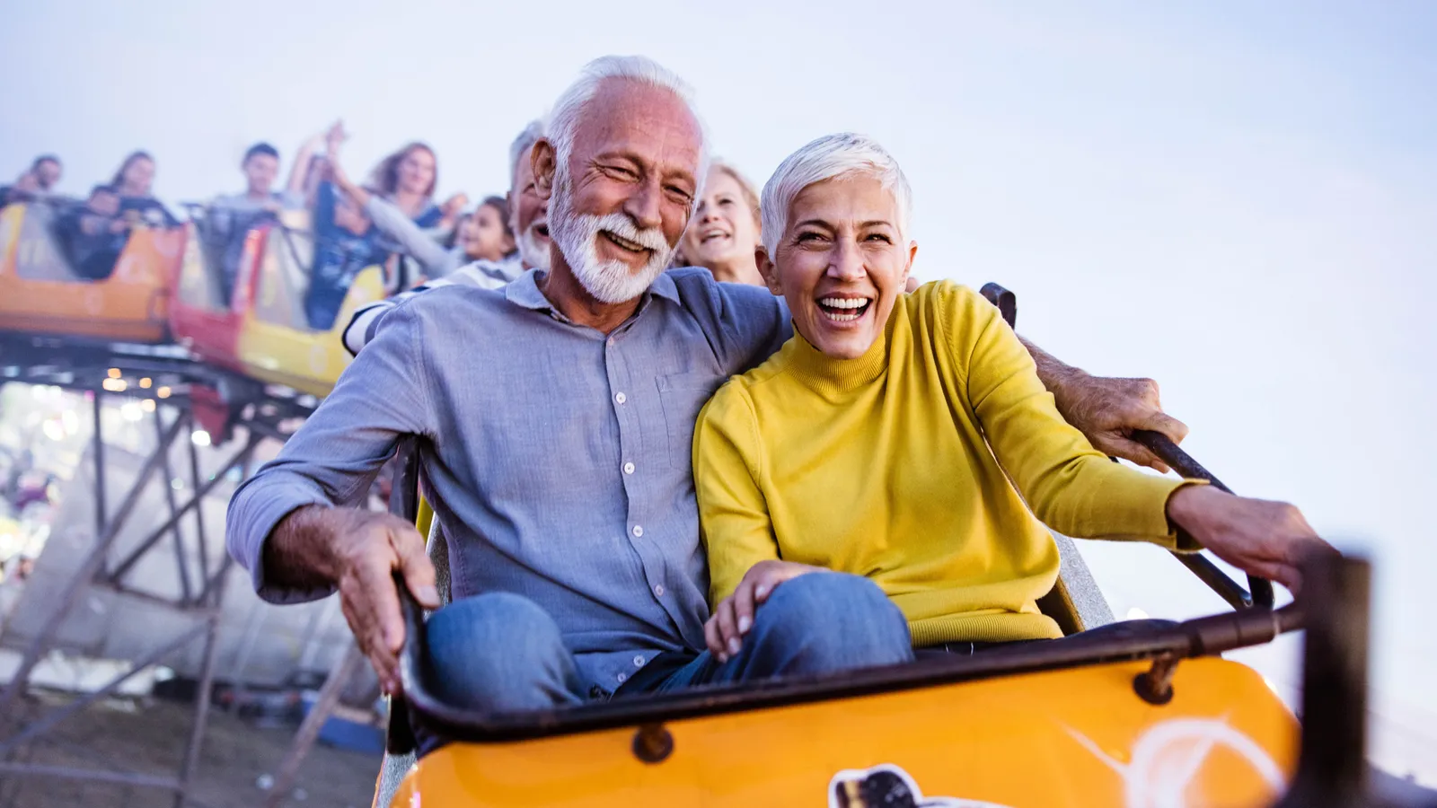 An older couple smiling on a rollercoaster, hands raised, conveying a sense of openness to a new chapter of life.