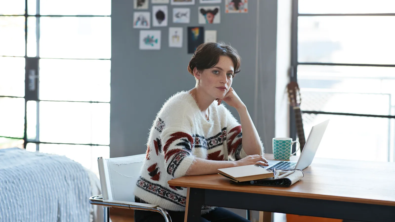 A person at a desk with their head in their hands beside a notebook and laptop.