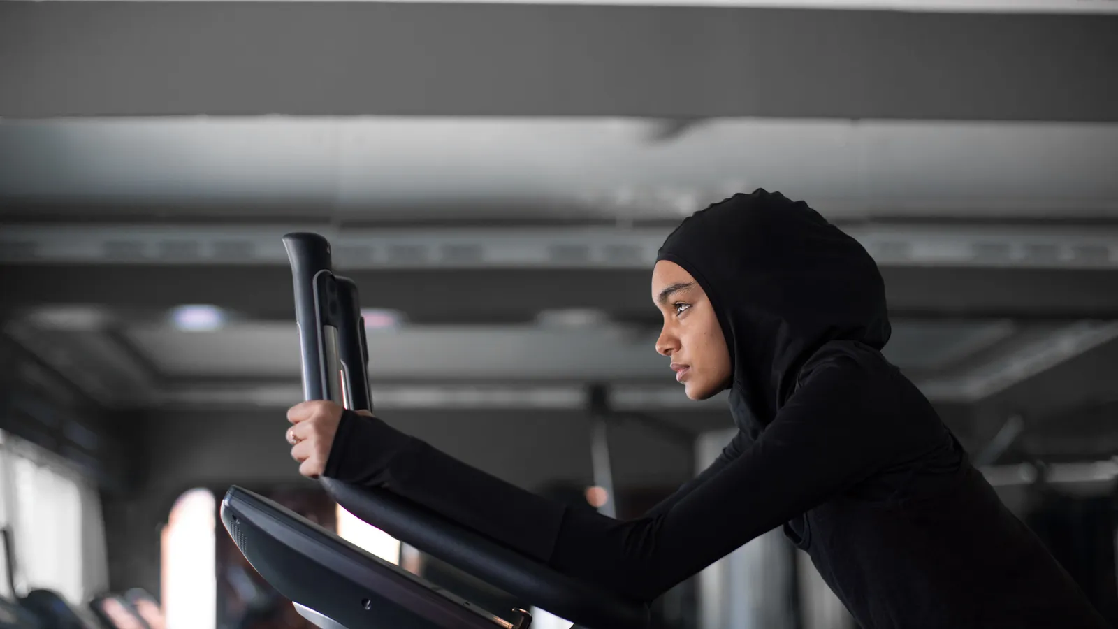 A woman in a hijab working out on an exercise bike in a gym.