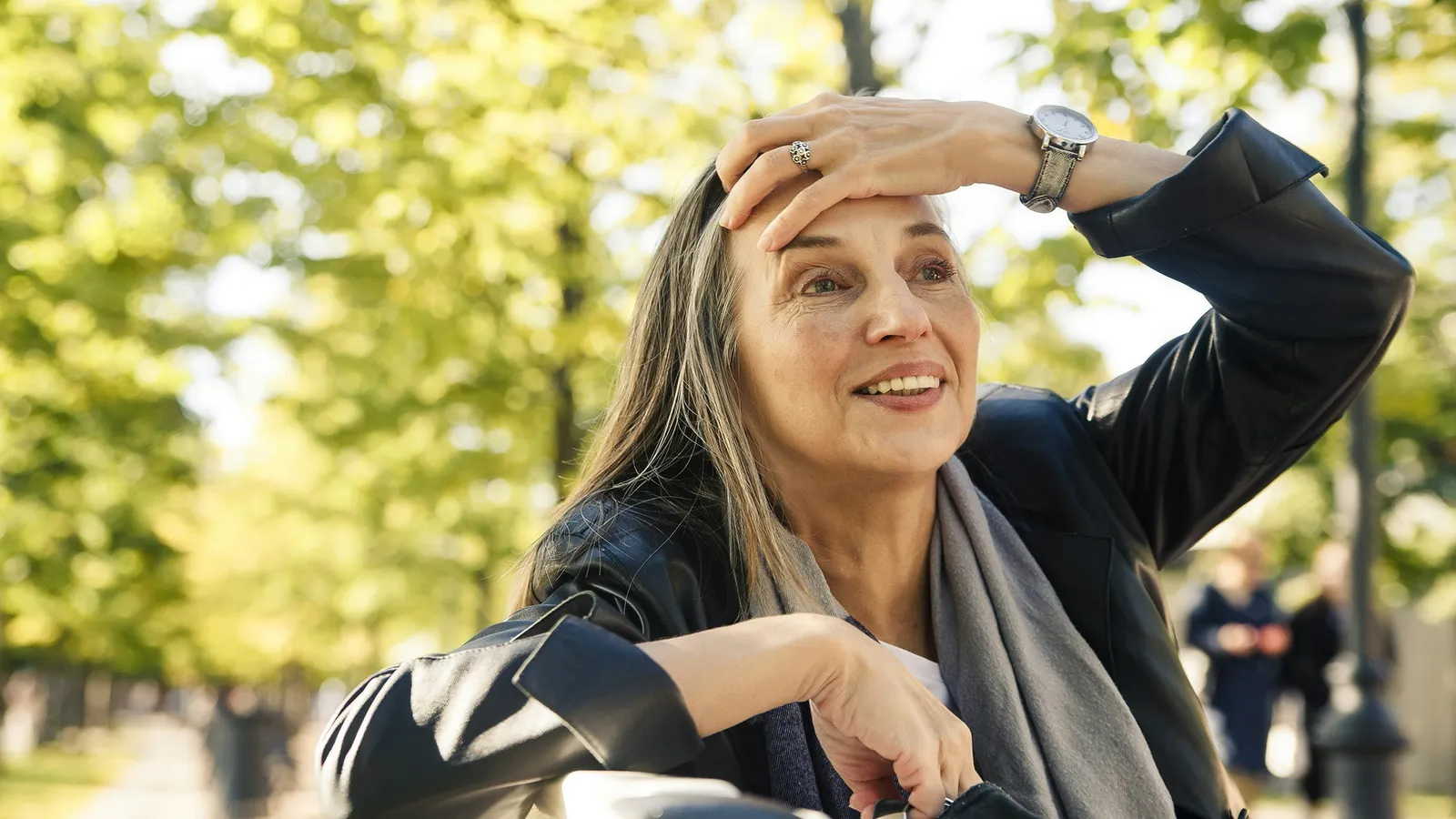 A woman shading her eyes and smiling in a sunlit park.